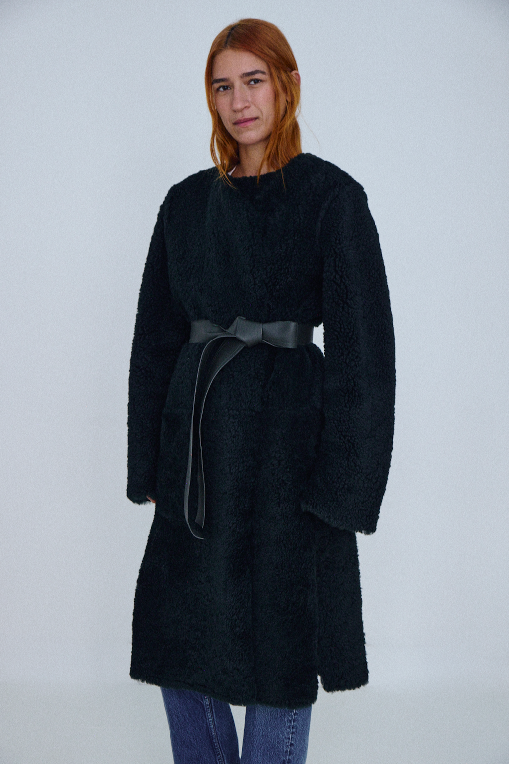 Person wearing a black coat with a belt on a white background