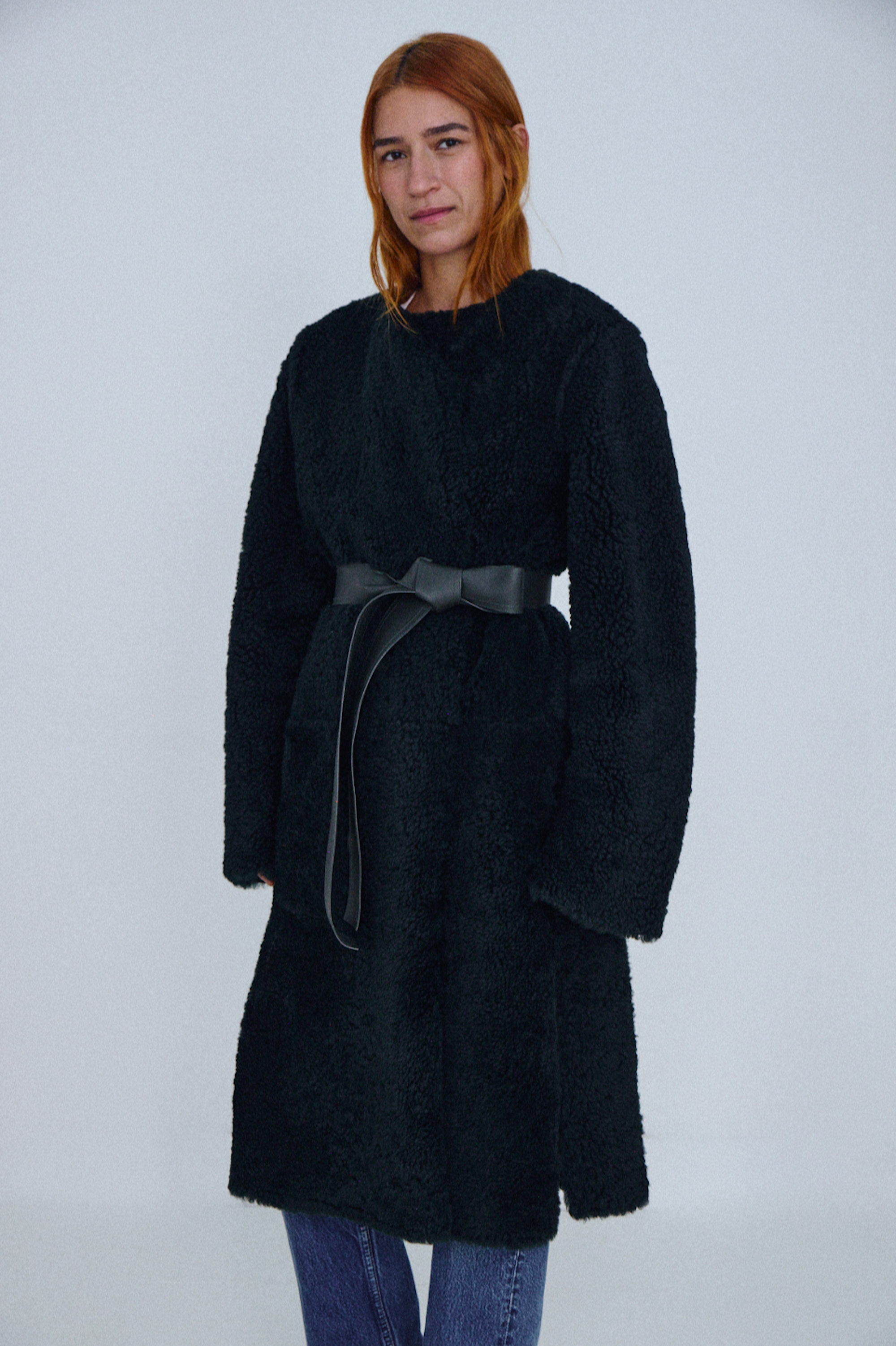 Person wearing a black coat with a belt on a white background